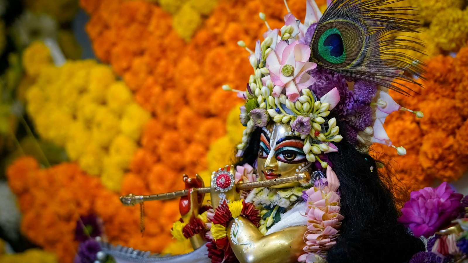 Colorful Krishna statue adorned with flowers and peacock feather, symbolizing Hindu spirituality.