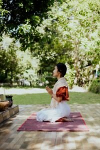 A woman kneeling outdoors, praying with a flower in a serene garden setting.